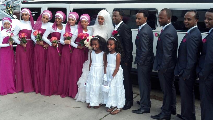 Somali American wedding party with brides maids, groomsmen and flower girls standing next to white Hummer Limo