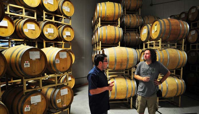 two men in storage room looking at bourbon barrels containing craft beer
